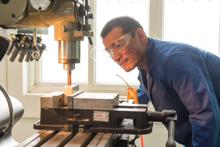 industrial machinist monitoring metal cutting process on vertical milling machine 768x512